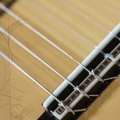 Ponte de guitarra acústica em madeira clara com cordas metálicas e detalhes decorativos