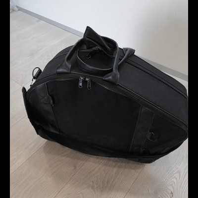 Mala preta de tecido com alças no chão de madeira clara