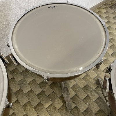 Tambor timpano com pele branca e aro metálico sobre chão de azulejos verde e bege