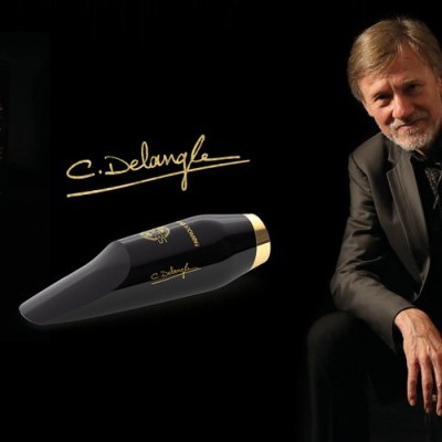 Palheta preta para instrumento com assinatura dourada C. Delangle e caixa preta ao lado de homem vestido de fato preto sentado