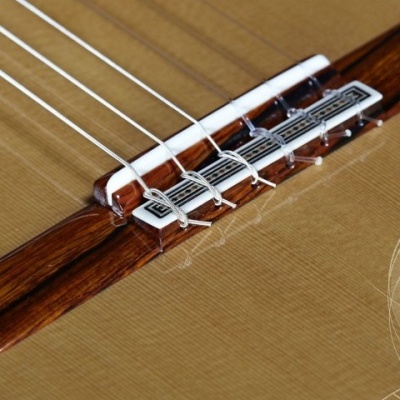 Close-up da ponte e cordas de guitarra clássica em madeira clara e escura