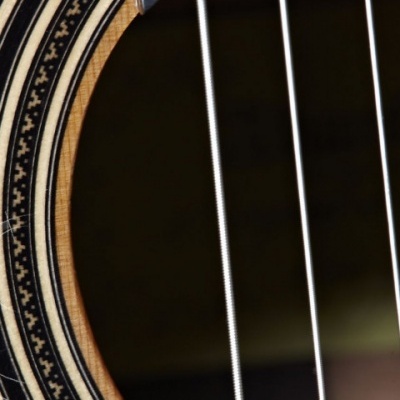 Close-up de parte do tampo e cordas de uma guitarra acústica em madeira clara com detalhes em preto e branco.