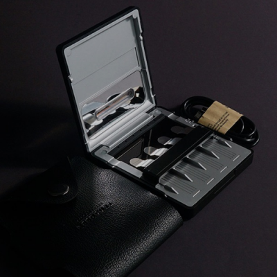 Estojo metálico cinza aberto com lâminas e bolsa preta de couro