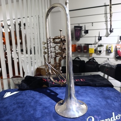 Trompete prateado sobre pano azul Vandoren numa loja de acessórios musicais