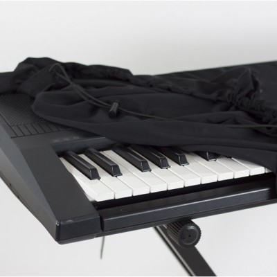 Teclado musical preto com tecido preto parcialmente cobrindo teclas numa estrutura metálica preta