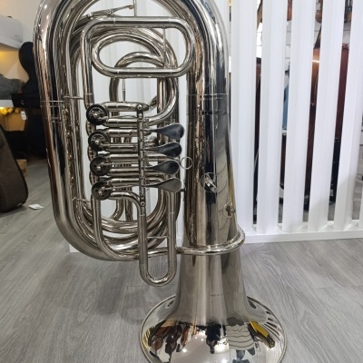 Eufónio metálico prateado com quatro pistões e corpo curvo sobre chão cinzento em loja.