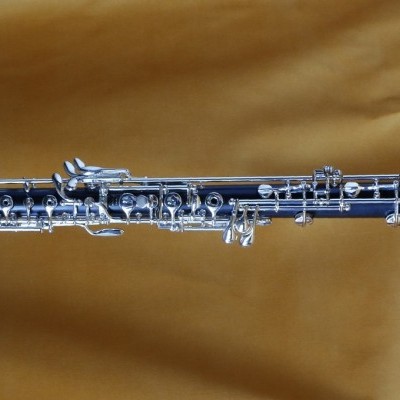 Oboé preta com chaves metálicas prateadas sobre fundo de tecido amarelo dourado.