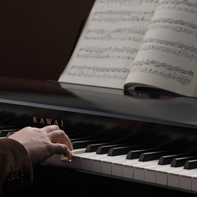 Piano digital preto da marca KAWAI com teclas e partitura, mãos tocando.