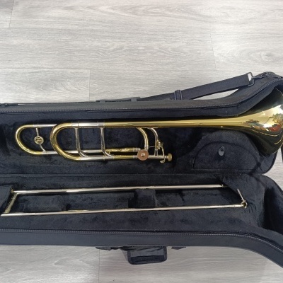 Trombone dourado em estojo preto acolchoado sobre chão de madeira cinza