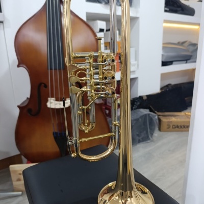 Trompete dourado com válvulas e tubos prateados sobre superfície preta, contrabaixo castanho ao fundo.