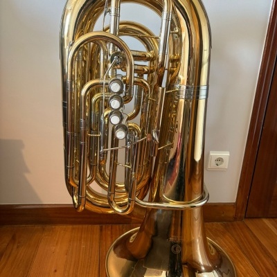 Tuba dourada com quatro válvulas em chão de madeira e parede branca