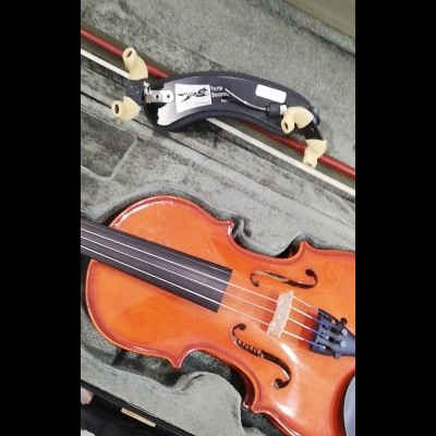 Violino laranja brilhante numa caixa cinzenta com suporte de ombro negro e bege