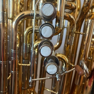 Instrumento de metal dourado com botões brancos e tubos curvos