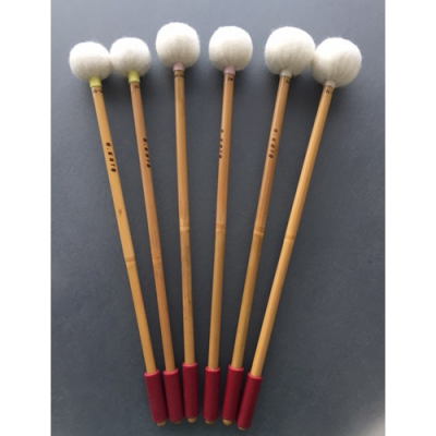 Seis baquetas de percussão com cabo castanho claro, ponta branca felpuda e base vermelha, sobre fundo cinzento.