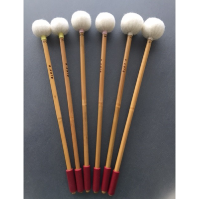 Seis baquetas com cabo de madeira, pontas de pelo branco e extremidades vermelhas sobre fundo cinzento