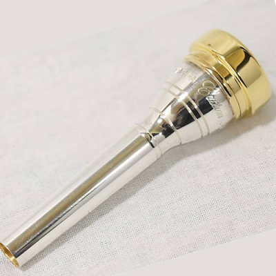 Boquilha metálica prateada e dourada para instrumento de sopro sobre tecido branco