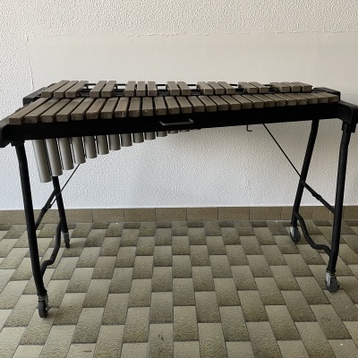 Xilofone de madeira com suporte metálico dobrável sobre chão padrão geométrico cinzento