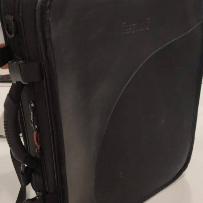 Mala preta rígida com alças e fechos exposta em loja com prateleiras atrás