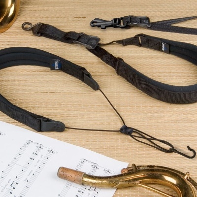 Colar preto acolchoado para saxofone com etiqueta Protec, sobre mesa de madeira com saxofone e partituras