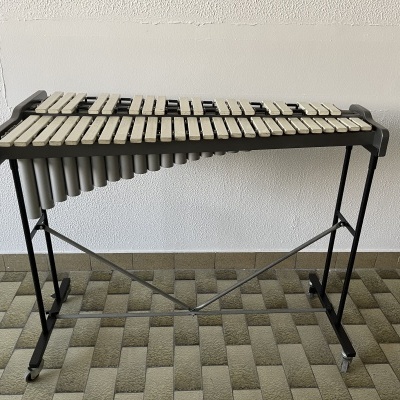 Xilofone com estrutura metálica preta e teclas brancas colocado contra parede branca