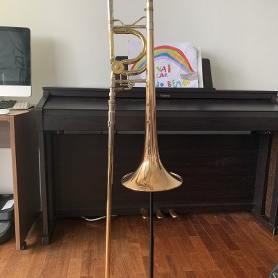 Trombone dourado em suporte com piano digital e cartaz colorido ao fundo