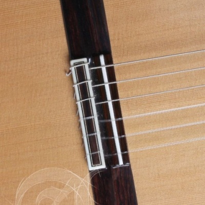 Ponte de guitarra acústica de madeira clara com seis cordas metálicas.