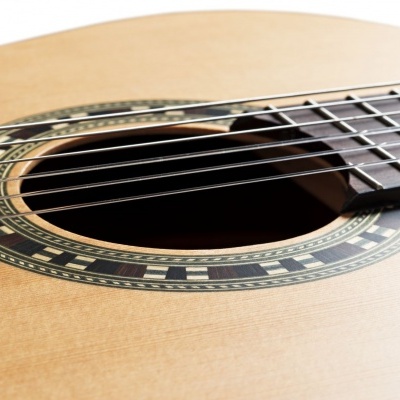 Close-up de guitarra acústica de madeira clara com seis cordas e roseta decorativa