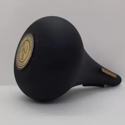 Selim preto de bicicleta com etiqueta redonda amarela em fundo cinzento.