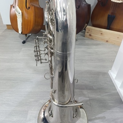 Tuba prateada polida em chão cinza com contrabaixos ao fundo