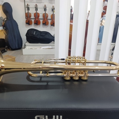 Trompete dourado sobre superfície preta com violinos e capas de instrumentos no fundo