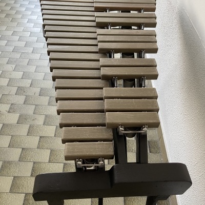 Instrumento musical de baloiço com barras de madeira castanhas numa base preta sobre azulejos cinza e bege