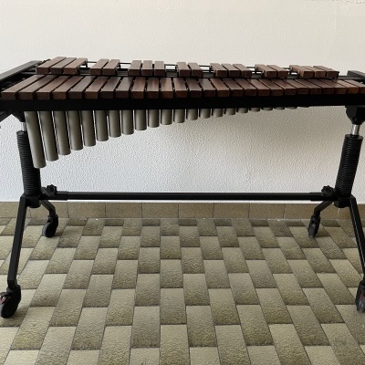Marimba com suporte preto e rodas sobre chão de azulejos cinzentos e bege