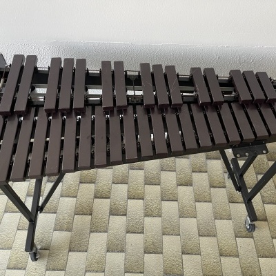 Marimba de madeira escura apoiada em tripé preto sobre piso geométrico.