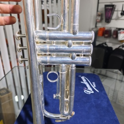 Trompete em metal prateado numa loja com tampo azul e logo Vandoren