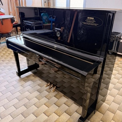 Piano vertical preto brilhante Yamaha com três pedais dourados num piso de azulejos bege