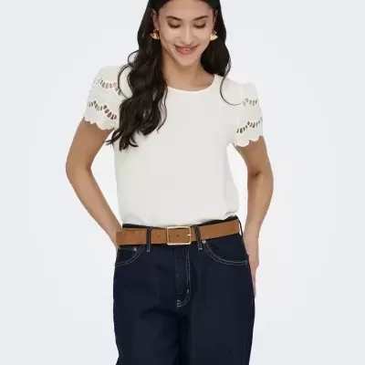 Mulher com blusa branca e calças de ganga azul escuro com cinto castanho.