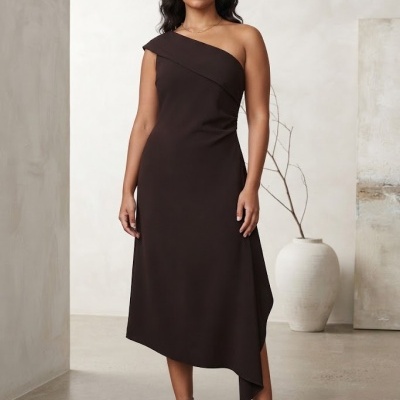 Mulher com vestido preto assimétrico e sandálias castanhas, em ambiente minimalista.