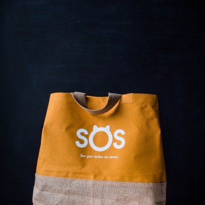 Mala de tecido amarelo e bege com texto SOS e frase em branco