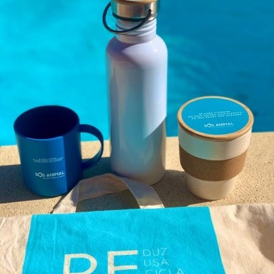 Produtos reutilizáveis brancos e azuis junto a piscina com garrafa, caneca, copo e toalha