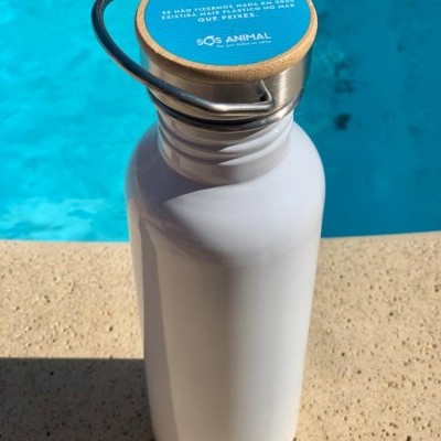 Garrafa metálica branca com tampa de madeira com texto azul e branco, à beira de uma piscina