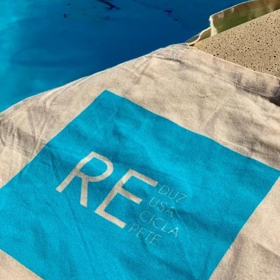 Tecido com estampa azul e texto branco junto a borda de piscina com água azul