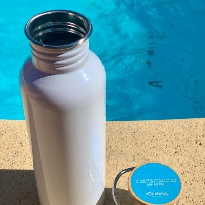 Garrafa térmica branca metálica e tampa azul com texto perto de piscina