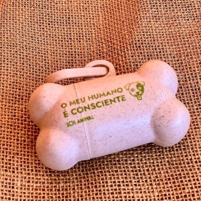 Dispenser bege em forma de osso para sacos com inscrição verde colocado sobre tecido de juta