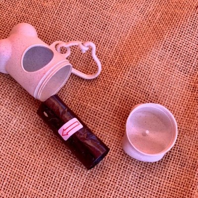 Garrafa dispensadora para sacos de lixo para cães com saco enrolado e tampa sobre tecido de juta.