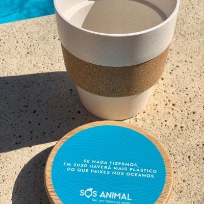 Copo reutilizável branco com faixa de cortiça e tampa de madeira com adesivo azul texto em português