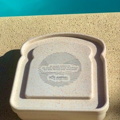 Caixa forma fatia de pão em material com aspeto natural e texto impresso no centro sobre superfície bege rugosa