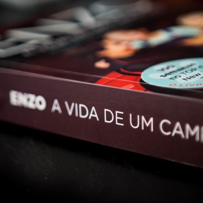 Livro 'ENZO A VIDA DE UM CAMPEÃO' com selo azul sobre superfície preta