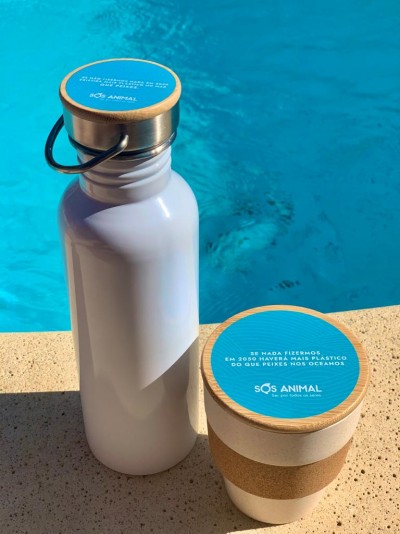 frasco metálico branco com tampa de madeira e copo reutilizável com tampa azul e suporte de cortiça junto à piscina