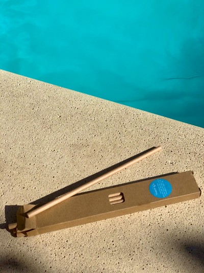 Conjunto de três palhinhas reutilizáveis de madeira em caixa de cartão junto à borda de uma piscina