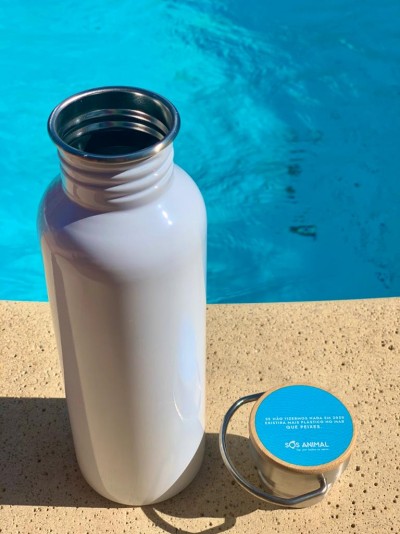 Garrafa térmica branca metálica e tampa azul com texto perto de piscina